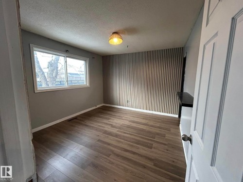 Empty room featuring wood finished floors, a textured ceiling, and an accent wall - 15016 80 Street, Edmonton, AB - Indoor Photo Showing Other Room