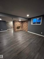 Finished basement featuring a fireplace, dark wood finished floors, and brick wall - 