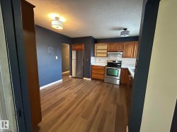 Kitchen featuring light countertops, open shelves, appliances with stainless steel finishes, brown cabinets, and a textured ceiling - 