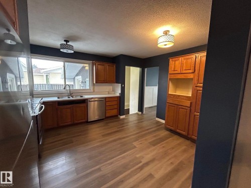 Kitchen featuring brown cabinets, dark wood finished floors, a textured ceiling, light countertops, and dishwasher - 15016 80 Street, Edmonton, AB - Indoor Photo Showing Kitchen With Double Sink