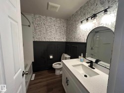 Full bathroom featuring shower / tub combination, wallpapered walls, vanity, a wainscoted wall, and dark wood-style flooring - 