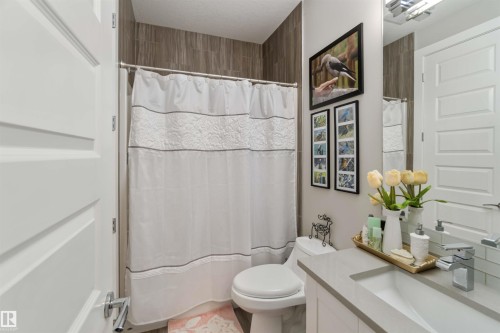 This bathroom features a shower area with tiled walls, a vanity with a rectangular sink, and a large mirror - 4 Lakeshore Cove, Beaumont, AB 