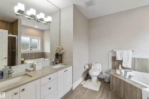 Bathroom featuring a dual vanity with light countertops, a rectangular bathtub with a tiled surround, and a mirror with an overhead light fixture - 4 Lakeshore Cove, Beaumont, AB 
