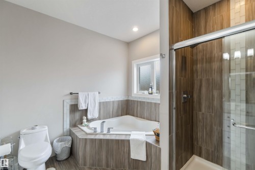 This property features a bathroom with a corner bathtub, a shower with a sliding glass door, and a window providing natural light - 4 Lakeshore Cove, Beaumont, AB 