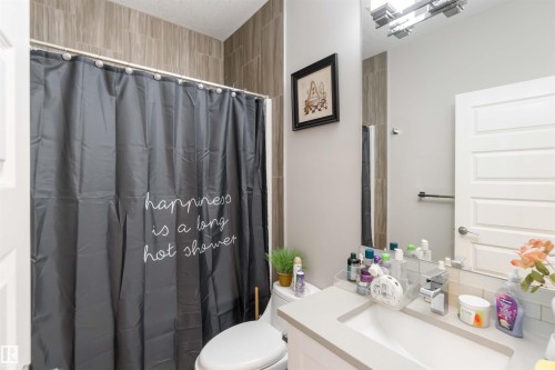 Bathroom featuring a vanity with a rectangular sink, a wall-mounted mirror, and a shower with tiled walls - 4 Lakeshore Cove, Beaumont, AB 