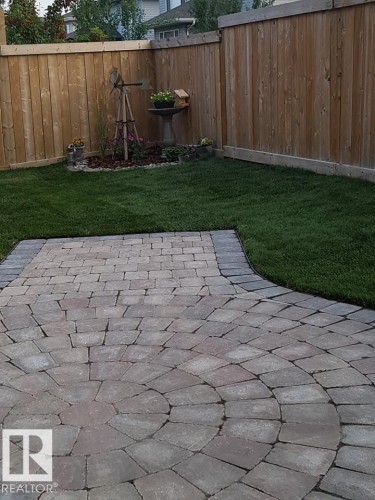 The property features a well-maintained lawn and a paved patio with a circular design - 4 Lakeshore Cove, Beaumont, AB 