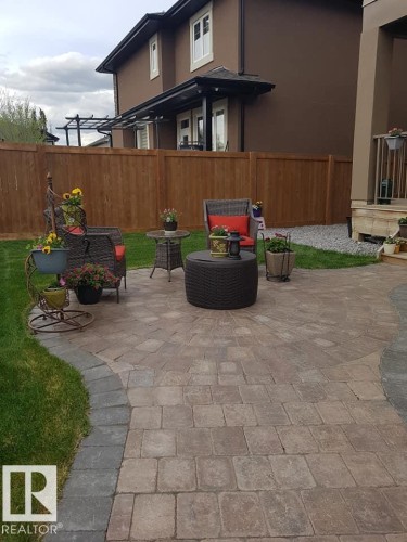 The property features a spacious paver patio with a decorative border, set against a well-maintained lawn - 4 Lakeshore Cove, Beaumont, AB 