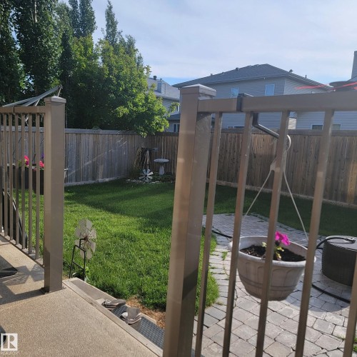 The property features a fenced yard with a lawn, mature trees, and a paved patio area - 4 Lakeshore Cove, Beaumont, AB 