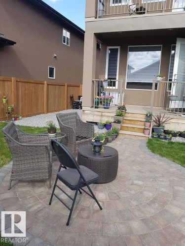 The property features a circular paver patio, a wooden fence, and a grassy area - 4 Lakeshore Cove, Beaumont, AB 