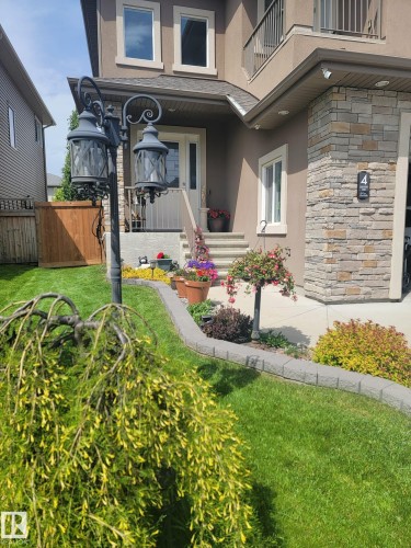 The property features a stucco exterior with stone accents, a well-maintained lawn, and a paved walkway leading to the front entrance - 4 Lakeshore Cove, Beaumont, AB 