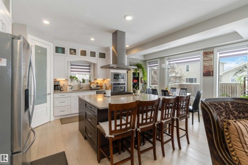 This kitchen features white cabinetry, stainless steel appliances, a large island with seating, and light-colored flooring - 4 Lakeshore Cove, Beaumont, AB 