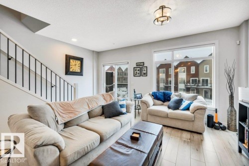 Living area featuring light-colored flooring, large windows, and a staircase with a black metal railing - 99 1010 Rabbit Hill Road, Edmonton, AB - Indoor Photo Showing Living Room With Fireplace
