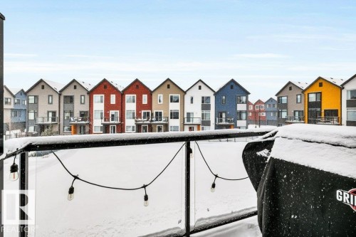 The property features a balcony with a glass railing and string lights, offering views of a row of houses with varied facade colors - 99 1010 Rabbit Hill Road, Edmonton, AB - Outdoor With Balcony