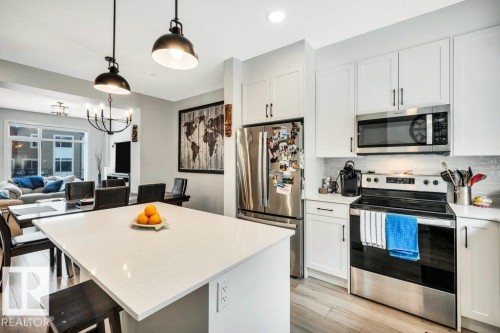 The kitchen features white cabinetry, stainless steel appliances, and a central island with a light-colored countertop - 99 1010 Rabbit Hill Road, Edmonton, AB - Indoor