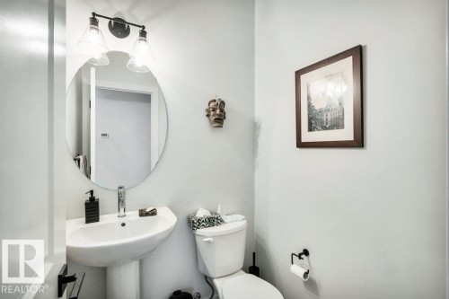 This powder room features a pedestal sink, a circular mirror, and a wall-mounted light fixture with two glass shades - 99 1010 Rabbit Hill Road, Edmonton, AB - Indoor Photo Showing Bathroom