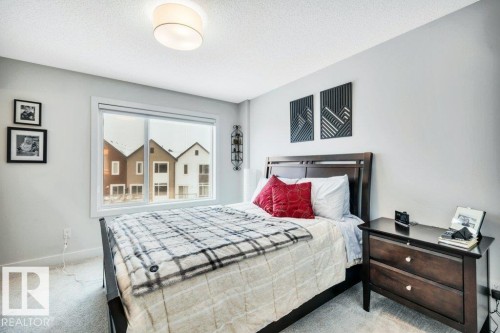 This room features light grey walls, a window overlooking residential properties, and a ceiling light fixture - 99 1010 Rabbit Hill Road, Edmonton, AB - Indoor Photo Showing Bedroom