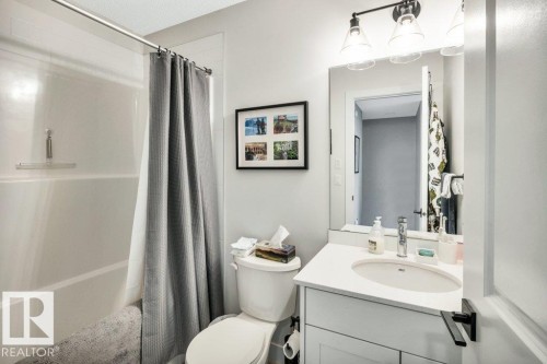 Bathroom featuring a white bathtub with a shower curtain, a toilet, and a vanity with an integrated sink and mirror - 99 1010 Rabbit Hill Road, Edmonton, AB - Indoor Photo Showing Bathroom