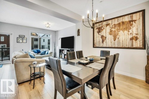 This open-concept living area features light-colored flooring, large windows providing natural light, and a dedicated dining space with a chandelier - 99 1010 Rabbit Hill Road, Edmonton, AB - Indoor Photo Showing Dining Room
