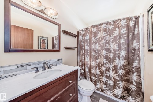 Bathroom featuring a dark wood vanity with a white countertop, a rectangular mirror with a dark wood frame, and a shower with a patterned curtain - 4237 116 Avenue, Edmonton, AB - Indoor Photo Showing Bathroom