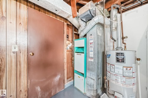 The utility area features a water heater and furnace, with wood paneling on the wall and a painted brown door - 4237 116 Avenue, Edmonton, AB - Indoor Photo Showing Basement