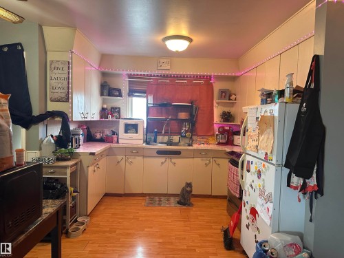 The kitchen features light-colored cabinetry, a refrigerator, and a window with a red curtain - 9724 102 Avenue, Westlock, AB - Indoor