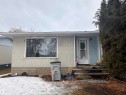 The property features an exterior with light-colored stucco and light blue siding, a front entry with a white door, and a mature evergreen tree - 9724 102 Avenue, Westlock, AB  - Outdoor 