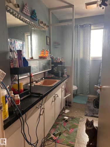 Bathroom featuring a vanity with an integrated sink, a wall-mounted mirror with overhead lighting, and a window providing natural light - 9724 102 Avenue, Westlock, AB - Indoor