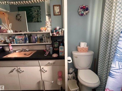 Bathroom with a toilet, a shower curtain featuring a botanical pattern, and a vanity with a pink sink, a dark countertop, and white cabinets - 9724 102 Avenue, Westlock, AB - Indoor Photo Showing Bathroom