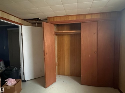 This room features wood paneling on the walls, a built-in wooden closet, and a white ceiling with visible tiles - 9724 102 Avenue, Westlock, AB - Indoor