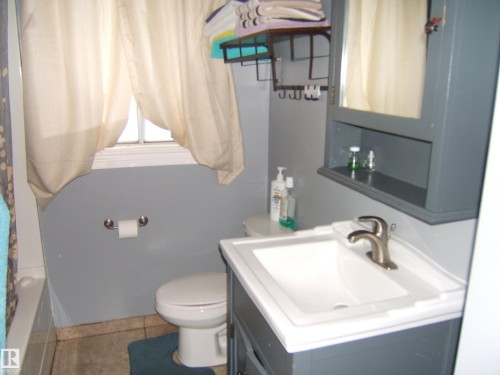 Bathroom featuring a single vanity with a white sink, a matching medicine cabinet, and a window with natural light - 5023 50 Street, Two Hills, AB - Indoor Photo Showing Bathroom