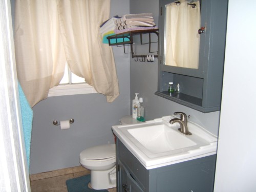 This bathroom features a vanity with a white sink, a mirror-front medicine cabinet, and a window with curtains - 5023 50 Street, Two Hills, AB - Indoor Photo Showing Bathroom