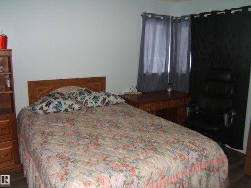 The room features a bed with a wooden headboard, light-colored walls, and a window with curtains - 5023 50 Street, Two Hills, AB - Indoor Photo Showing Bedroom