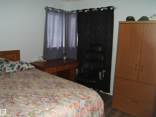The room features light blue walls, a wooden bed frame, and wood-look flooring - 5023 50 Street, Two Hills, AB - Indoor Photo Showing Bedroom