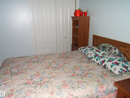 The room features light blue walls, a wooden headboard, and white bi-fold closet doors - 5023 50 Street, Two Hills, AB - Indoor Photo Showing Bedroom