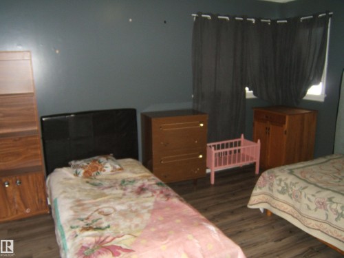 The room features durable wood-look flooring and a window with dark privacy curtains - 5023 50 Street, Two Hills, AB - Indoor Photo Showing Bedroom