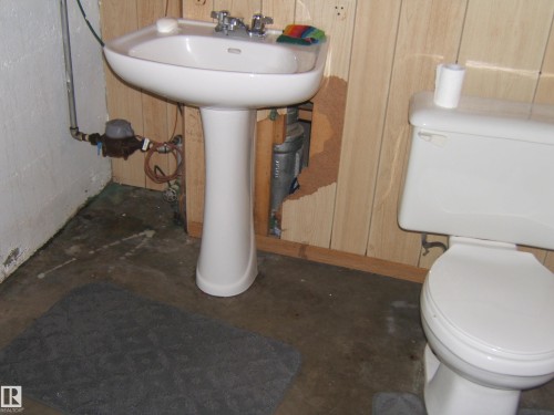 Bathroom featuring a white pedestal sink, a white toilet, and wood paneling on the wall - 5023 50 Street, Two Hills, AB - Indoor Photo Showing Bathroom