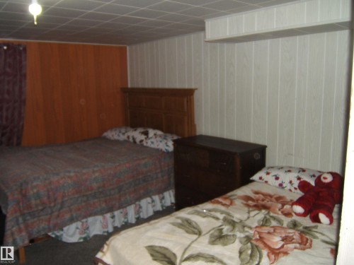 The room features wood paneling on the walls, a drop ceiling, and carpeted flooring - 5023 50 Street, Two Hills, AB - Indoor Photo Showing Bedroom