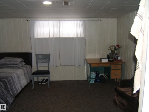 This room features a window with white curtains, recessed ceiling lighting, and wall paneling - 5023 50 Street, Two Hills, AB - Indoor Photo Showing Bedroom