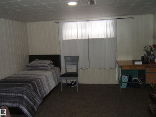 The room features paneled walls and a window with white curtains - 5023 50 Street, Two Hills, AB - Indoor Photo Showing Bedroom