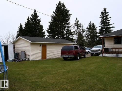 Spacious backyard featuring a manicured lawn, detached accessory building with a single door entry, and mature evergreen trees - 5023 50 Street, Two Hills, AB - Outdoor