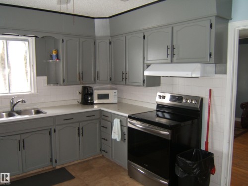 The kitchen features grey cabinetry, white countertops, a double basin stainless steel sink, and a white tile backsplash - 5023 50 Street, Two Hills, AB - Indoor Photo Showing Kitchen With Double Sink