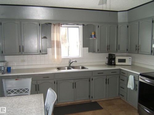 The kitchen features extensive grey cabinetry, a white tiled backsplash, and a double basin stainless steel sink - 5023 50 Street, Two Hills, AB - Indoor Photo Showing Kitchen With Double Sink