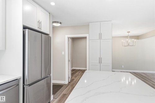 The kitchen features a spacious island with a white countertop, white cabinetry with silver hardware, and a stainless steel refrigerator - 11 Sonora Drive, St. Albert, AB - Indoor Photo Showing Kitchen