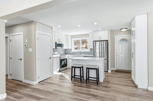 Open concept kitchen with wood-look flooring, white cabinetry, stainless steel appliances, and a central island with bar seating - 11 Sonora Drive, St. Albert, AB - Indoor Photo Showing Kitchen With Stainless Steel Kitchen With Upgraded Kitchen