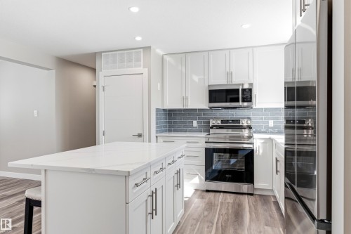 Modern kitchen featuring white cabinetry, a spacious island with a white countertop, stainless steel appliances, and wood-look flooring - 11 Sonora Drive, St. Albert, AB - Indoor Photo Showing Kitchen With Stainless Steel Kitchen With Upgraded Kitchen