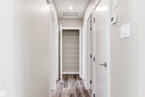 Hallway with light-colored walls and dark wood-style flooring, featuring several white doors, a ceiling light, and a thermostat - 11 Sonora Drive, St. Albert, AB - Indoor Photo Showing Other Room