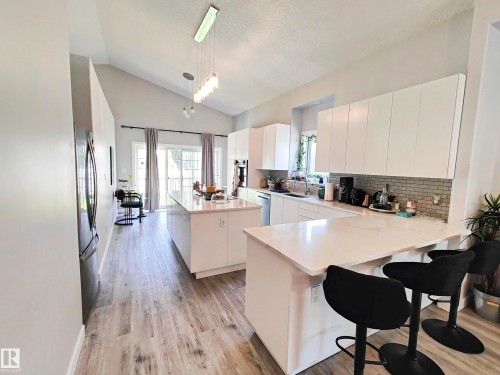 The kitchen features a vaulted ceiling, white cabinetry, a light-colored subway tile backsplash, and light wood-style flooring - 215 Peter Close Nw, Edmonton, AB - Indoor Photo Showing Kitchen With Double Sink