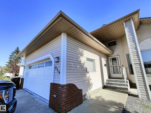 The property features light-colored horizontal siding, a white garage door with upper windows, and a front entrance with a white door and steps - 215 Peter Close Nw, Edmonton, AB - Outdoor