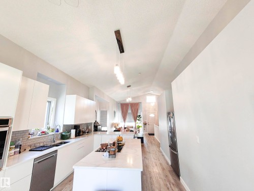 The property features a kitchen with white cabinetry, a kitchen island with a cooktop, and a stainless steel dishwasher - 215 Peter Close Nw, Edmonton, AB - Indoor