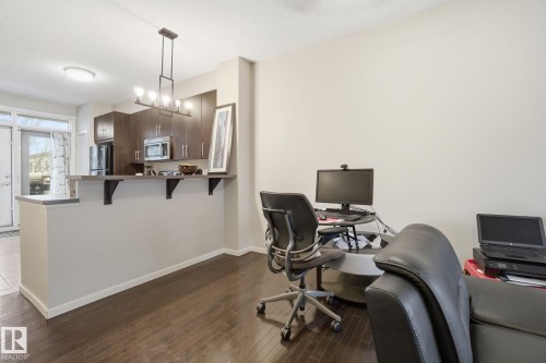 The property features dark hardwood flooring throughout this space, an open-plan kitchen area with dark cabinetry, stainless steel microwave, and a breakfast bar with decorative supports - 75 603 Watt Boulevard, Edmonton, AB - Indoor Photo Showing Office